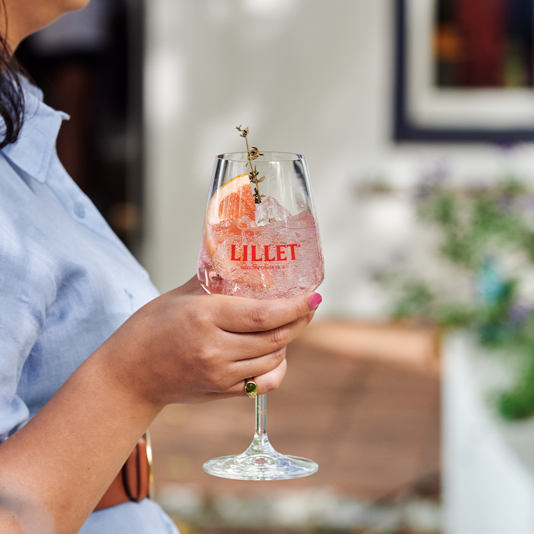 girl holding glass with lillet pink spritz garnished with grapefruit and thyme